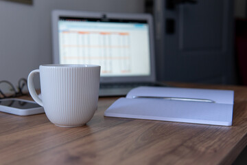a cup of coffee close-up on the background of a laptop and a notepad with a pen. coffee break composition during work.