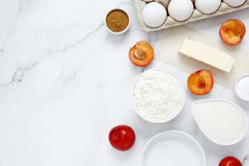Ingredients for making classic cake pie with plums on white background. Concept homemade food, seasonal pastries. Top view, copy space