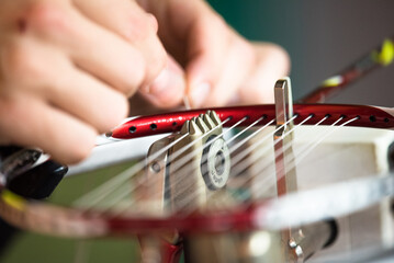 Closeup of a Japanese badminton weaving machine for repairing of broken badminton strings - a male hand weaves strings in a badminton racket head.