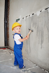 Full length of baby boy holding hammer and looking at camera while standing by the wall. Kid...