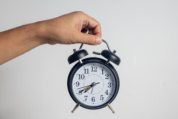 The man holds an alarm clock, against a white background.