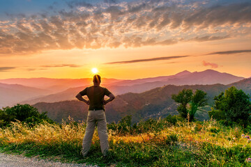 rejoicing man with beautiful scenic mountain sunset landscape on background. happy man watching amazing evening sunset