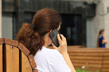 Woman talking on smartphone sitting on a street bench. Using mobile phone in summer city