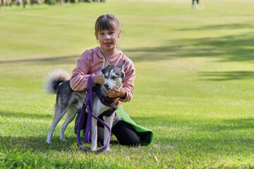 Teen girl smiling hugs husky dog lying on green grass on summer