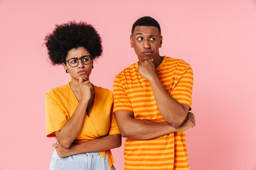 African american man and woman looking away and touching chin while standing isolated over pink background