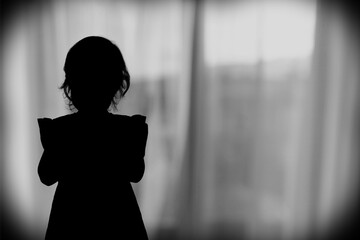 Silhouette of sad small child on window background