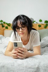 Young woman casually lying in bed, using her phone