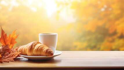 A cup of coffee and croissant on a wooden table with an autumn blurred background with a place for...