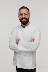 Studio portrait of a young man, a cook, in a tunic, who smiles on a white background.