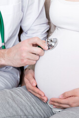 Doctor is checking pregnant woman's belly with a stethoscope. Physician is listening to a heartbeat of a baby