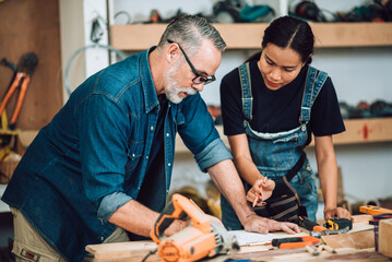 Small business furniture owner and professional architect interior designer working together in carpenter workshop with blueprint and tablet discussing about home furnishing design project..
