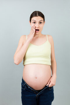 pregnant woman in unzipped jeans showing her naked belly at colorful background with copy space. Baby expecting concept