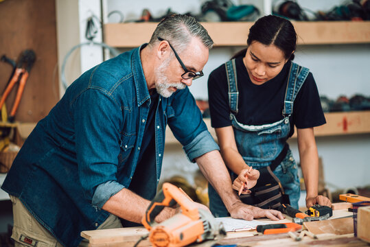 Small business furniture owner and professional architect interior designer working together in carpenter workshop with blueprint and tablet discussing about home furnishing design project..