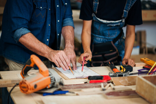 Small business furniture owner and professional architect interior designer working in carpenter workshop with blueprint and tablet discussing about home furnishing design project.