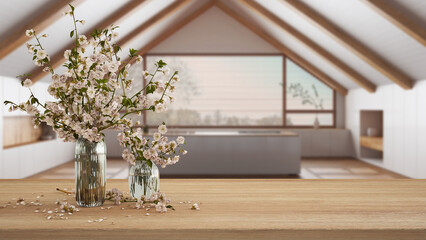 Wooden table, desk or shelf close up with branches of cherry blossoms in glass vase over blurred view of japandi kitchen, minimalist interior design concept