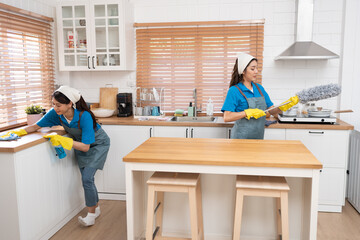 Two Asia woman in workwear maid cleaning home and holding dusting brush in her hand and wiping with microfiber cloth in kitchen room at home