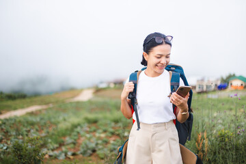 Backpacker woman using smartphone on village and fog background. Young female traveler searching internet during vacation trips. booking and planning for a trip.