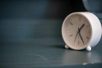 White alarm clock sitting on a blue shelf, the clock is small in size