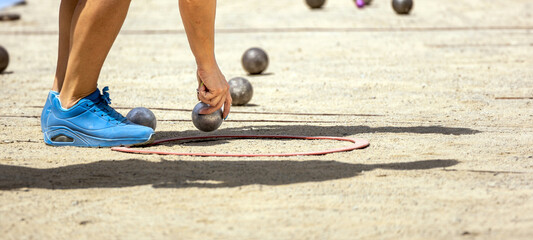 Hand of young sporty woman in sports shoes catching metal petanque ball to compete in qualifying...