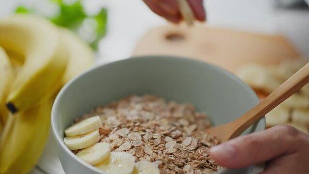 Cereal, a woman housewife adds a ripe banana to a bowl of oatmeal porridge in a home kitchen. active caucasian woman regularly following the right diet, uses modern methods of cooking, female