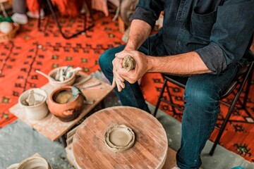 Male potter working on a clay object using his hands on a wooden wheel