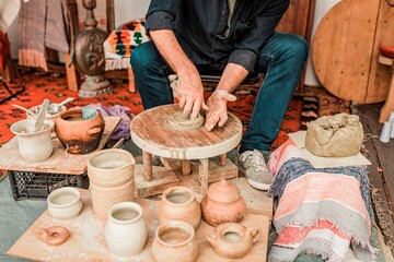 Male potter working on a clay object using his hands on a wooden wheel