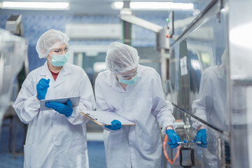 Female factory workers check machine systems at the industrial factory. Women working in clean rooms for beverage and food production