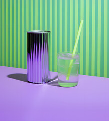 Nice drink can, straw and glass, striped green wallpaper in the background, summer outfit, contemporary style.