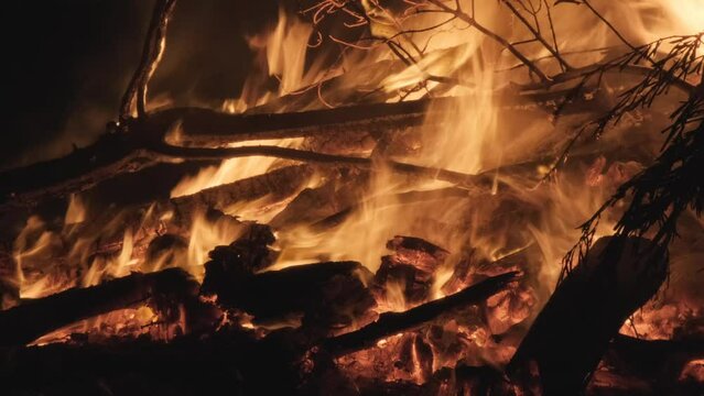 A pyre of wooden logs burning, orange fire flames from a campfire at night, zoom out.
