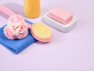 Obraz na płótnie Canvas Ecological bathing products on a purple background. Natural pink soap on a white soap dish, a blue washed shower towel and pink brush with a long handle for body care. Copy space for text.