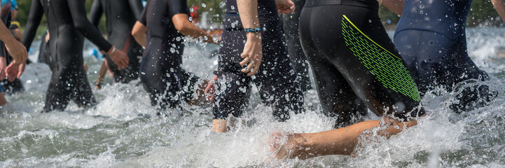Athletes in wetsuits running into a lake at a triathlon competition