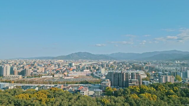 [Drone] Over the blue sky and the forest that spreads all over, go slowly while taking aerial shots of the cityscape