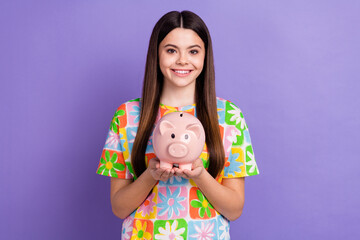 Photo portrait of attractive teen woman hold piggy bank money dressed stylish flower print clothes isolated on purple color background