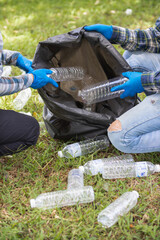 Two man employees use black garbage bags to collect plastic bottles and recyclable waste from the lawn and sidewalks for recycling. Concept of sorting plastic waste for recycling