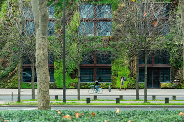 A cyclist and a pedestrian cross in front of the vegetal walls of  Musee du Quai Branly in Paris