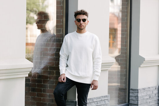 Man wearing white sweatshirt or hoodie for mock up, logo designs or design prints with with free space on the city streets.