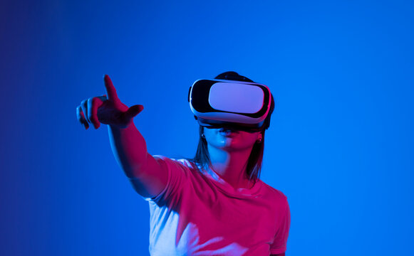 Brunette woman in VR headset looking up at the objects in virtual reality. VR is a computer technology that simulates a physical presence and allows the user to interact with environment.