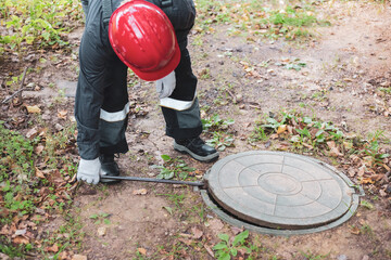 a man in overalls opens a sewer hatch. Cleaning of sewers and drains