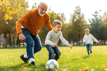 Happy family boy playing football soccer with grandfather at public park at sunset summer day. Healthy active sport for young family.