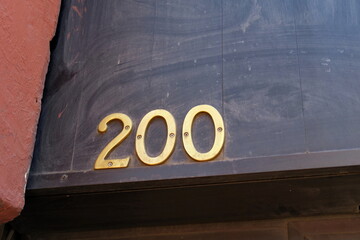 Numéro 200. Numéro de rue. Chiffres dorés sur fond sombre.