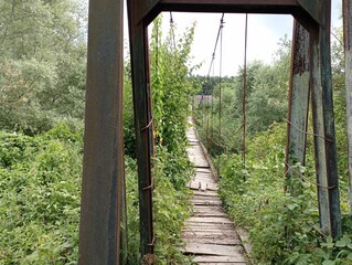 Pedestrian suspension old bridge across the river. Dangerous passage through water.