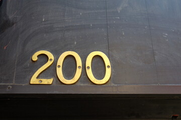 Numéro 200. Numéro de rue. Chiffres dorés sur fond sombre.