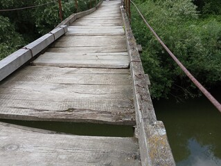 Obraz premium An extreme river crossing made of old rotten boards. Suspension bridge for pedestrians.