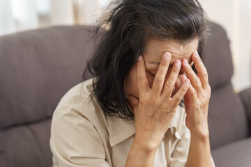 Sad middle age Asian woman touching forehead having headache suffering from migraine. mature asian woman feeling sick or depression.