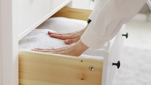 A housewife folds clean bedding or white towels after washing into a laundry box in a chest of drawers. Organization and storage of home comfort in the house	
