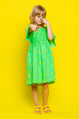 I am watching you. Young blonde school girl pointing at her eyes and camera, show I am watching you gesture, spying on someone. Preteen female child kid isolated on studio yellow background. Vertical