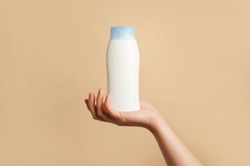 Woman holding white bottle of lotion or shampoo in her hand, gray background with copy space