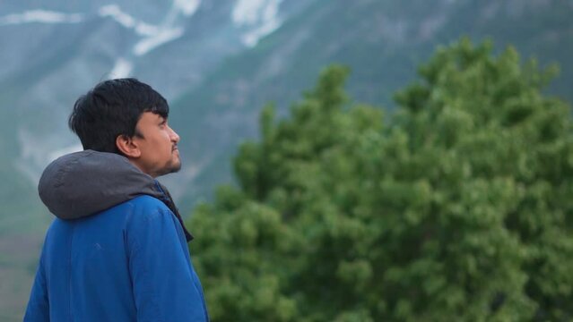 Person looking at the mountains. Young Indian man looking at mountains with hopeful eyes. Confident Indian man outdoors. Man wearing warm winter jacket in mountains. 