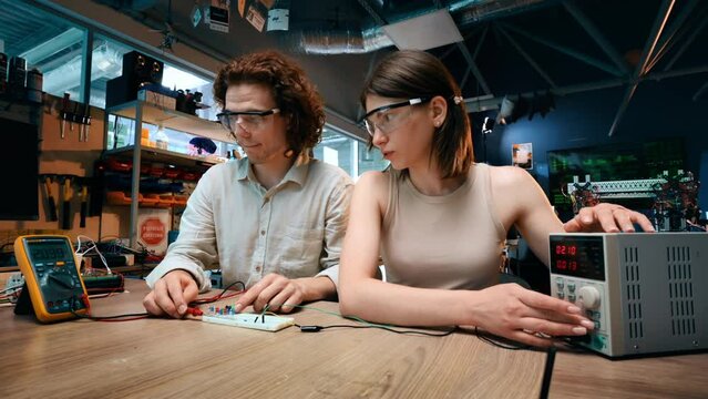 Young man and woman in protective glasses doing experiments with electricity in a laboratory. Tools on the table