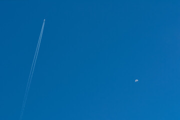 Blue clear sky with a flying airplane and a half-full moon